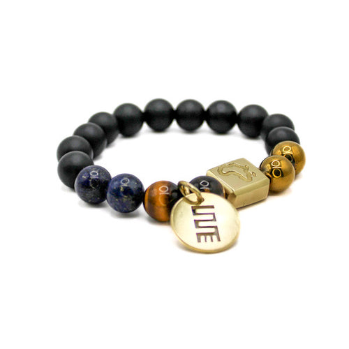 Blue Owula Made In Africa beaded bracelet with NKYINKYIM Adinkra symbol pendant, handcrafted in Ghana using gold-plated hematite beads, tiger eye, black frosted glass beads and blue lapis lazuli beads. Nkyinkyim Adinkra symbol means twisting of the journey of life.
